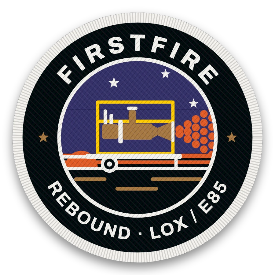 Firstfire mission patch, 3 inch embroidered: the LOX/E85 test engine in its yellow cage on a trailer stand, firing a dot plume at dusk, FIRSTFIRE across the top and REBOUND · LOX / E85 around the bottom